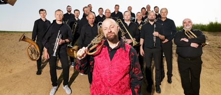 Eine Gruppe von Musikern posiert für ein Foto im Freien. Sie halten verschiedene Instrumente wie Trompeten und Posaunen.