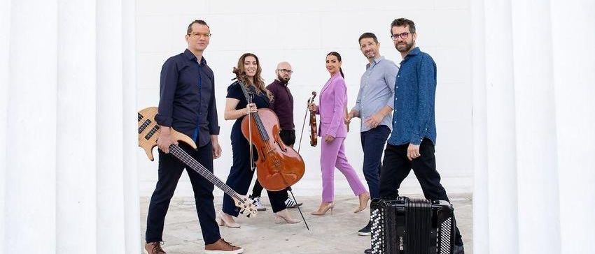 Eine Gruppe von Musikern posiert mit ihren Instrumenten für ein Foto in einem weiß gestrichenen Raum.