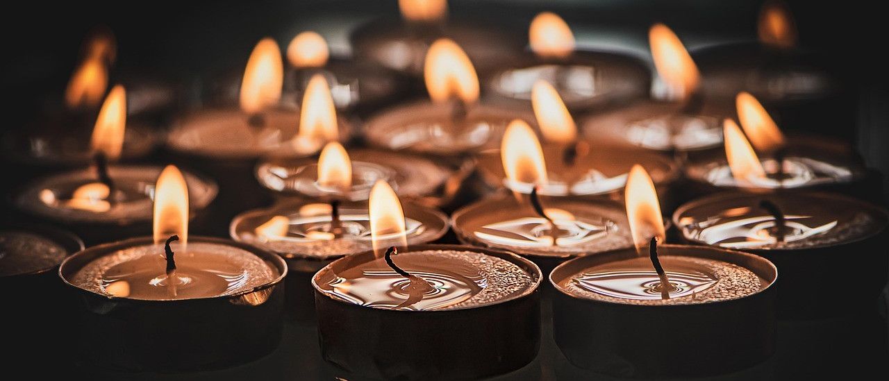 Eine Sammlung entzündeter Kerzen mit geschmolzenem Wachs auf schwarzen Haltern, die warmes Licht und sanfte Schatten auf einem dunklen Hintergrund werfen.