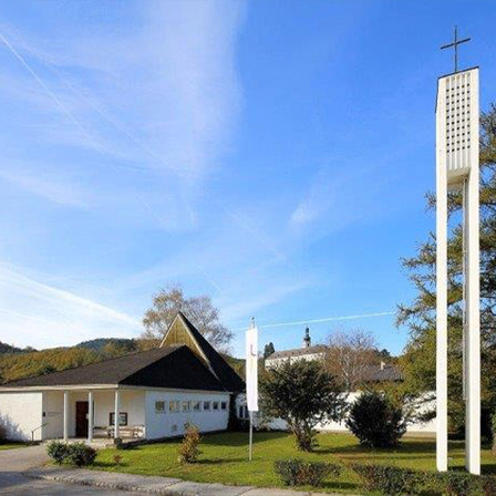 Eine weiße Kirche mit schwarzem Dach steht unter blauem Himmel, mit einem hohen weißen Turm in der Nähe.