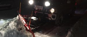 Ein schwarzer SUV mit Schneepflugaufsatz räumt bei Nacht Schnee in einem verschneiten Bereich. Das Kennzeichen lautet LN 683 CP.