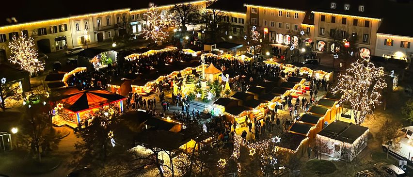 Ein geschäftiger Weihnachtsmarkt bei Nacht, geschmückt mit funkelnden Lichtern und festlichen Dekorationen, mit zahlreichen Menschen, die zwischen Ständen umherwandern und die Atmosphäre genießen.