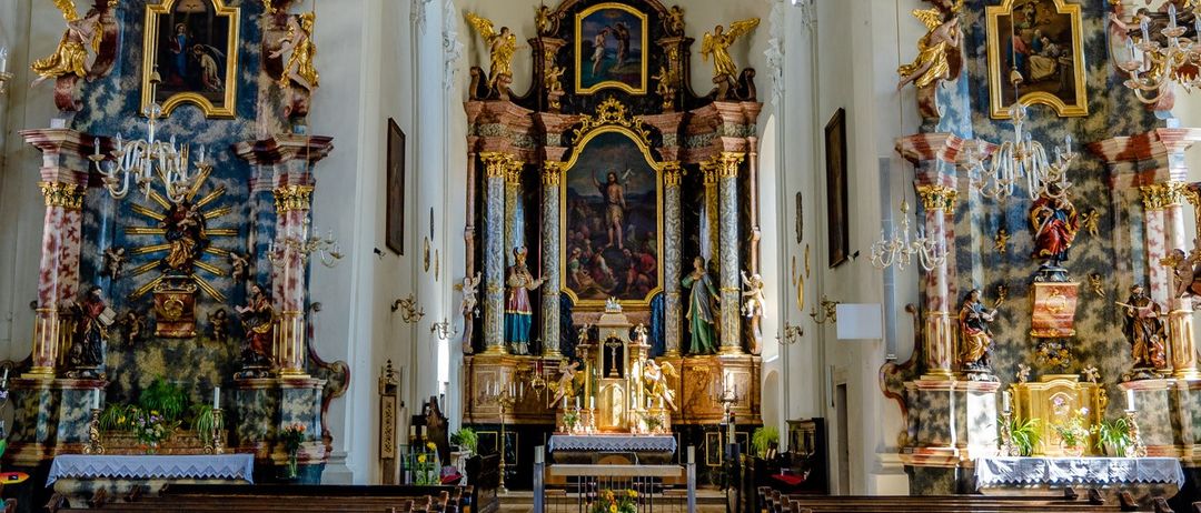 Eine Kircheninnenansicht mit kunstvollen goldenen Altären, Statuen und religiösen Gemälden sowie Reihen hölzerner Kirchenbänke.