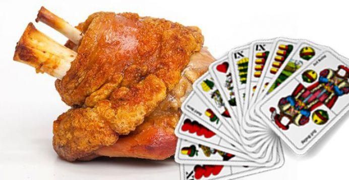 Ein gebratenes Fleischgericht mit Knochen, serviert neben einer Sammlung von Spielkarten auf weißem Hintergrund.