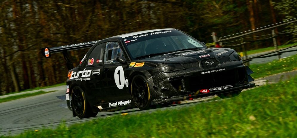 A black race car with the number 1 on the side drives on a racetrack. The car has a carbon fiber spoiler and a sponsor logo on the side.