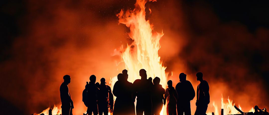 Mehrere Personen stehen um ein großes Lagerfeuer herum, die Flammen beleuchten ihre Silhouetten gegen den dunklen Nachthimmel.