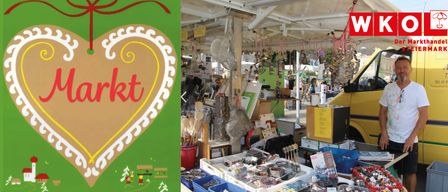 A market stall with a heart-shaped sign, various items for sale, and people browsing in the background.