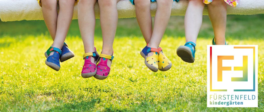Vier Kinder in passenden Outfits sitzen auf einer Bank in einem Grasbereich. Sie tragen Sandalen mit bunten Mustern.