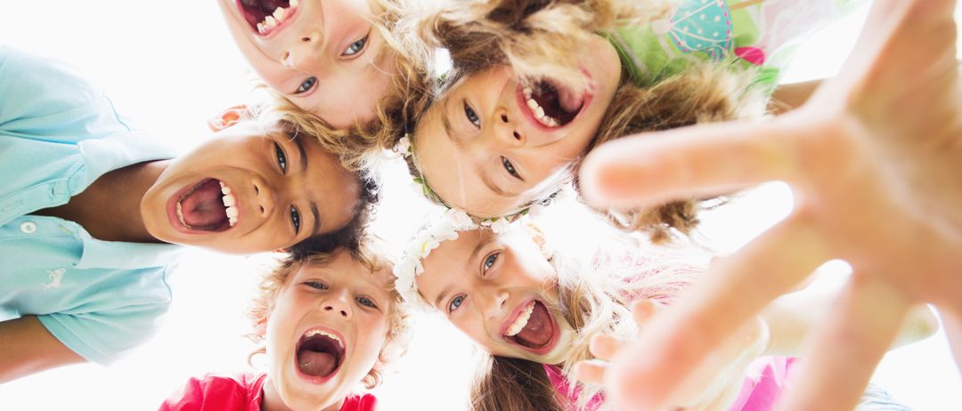 Eine Gruppe junger Kinder, die lächeln und lachen, stehen im Kreis. Jedes Kind trägt verschiedene Kleidung. Einige haben Blumen in den Haaren.