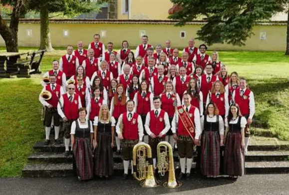 Ein Musikverein in traditionellen Kostümen posiert mit Musikinstrumenten vor einem Gebäude.