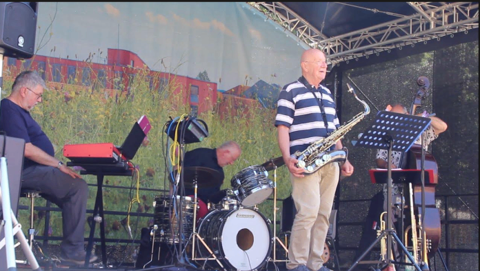Eine Band spielt auf der Bühne mit einem Saxophonisten, einem Mann am Keyboard, einem Schlagzeuger und einem Cellisten im Hintergrund.