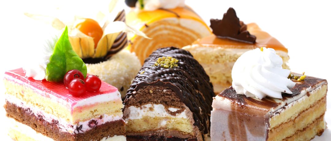 Eine Auswahl an Desserts ist auf einem weißen Hintergrund ausgestellt. Dazu gehören geschichtete Kuchen, ein Schokoladenroll und ein quadratischer Kuchen mit weißer Glasur.