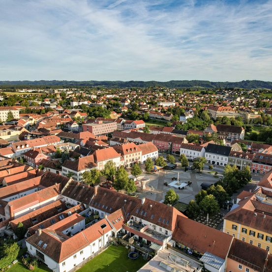 Eine Luftaufnahme einer Stadt mit vielen Gebäuden, hauptsächlich mit roten Dächern, vor dem Hintergrund von Bergen und einem klaren blauen Himmel.