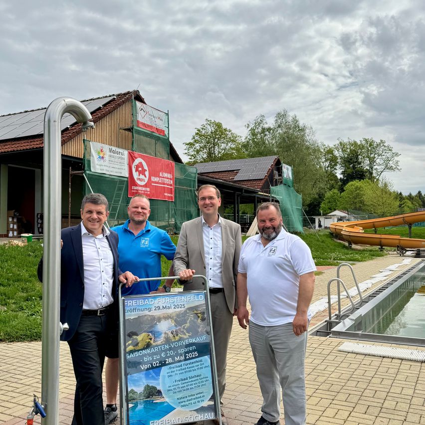 Vier Männer stehen draußen in der Nähe eines Pools. Sie lächeln und scheinen für ein Foto zu posieren. Hinter ihnen steht ein Haus mit Solarpanelen.