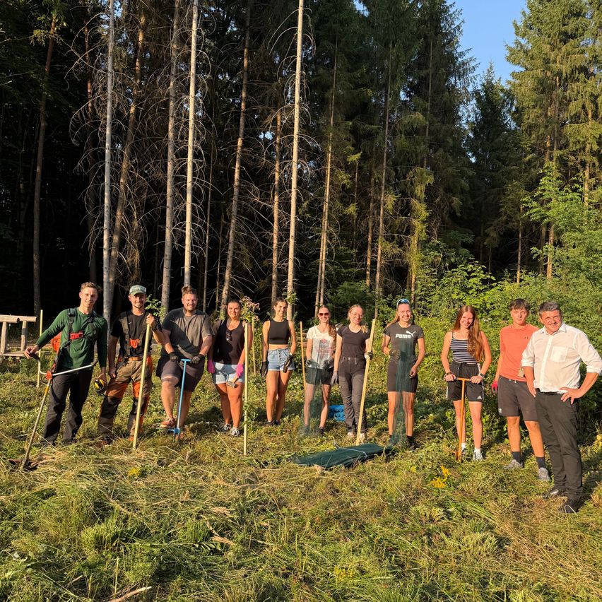 Eine Gruppe von Menschen steht auf einem Feld und hält Werkzeuge in der Hand. Sie lächeln und scheinen für ein Foto zu posieren.