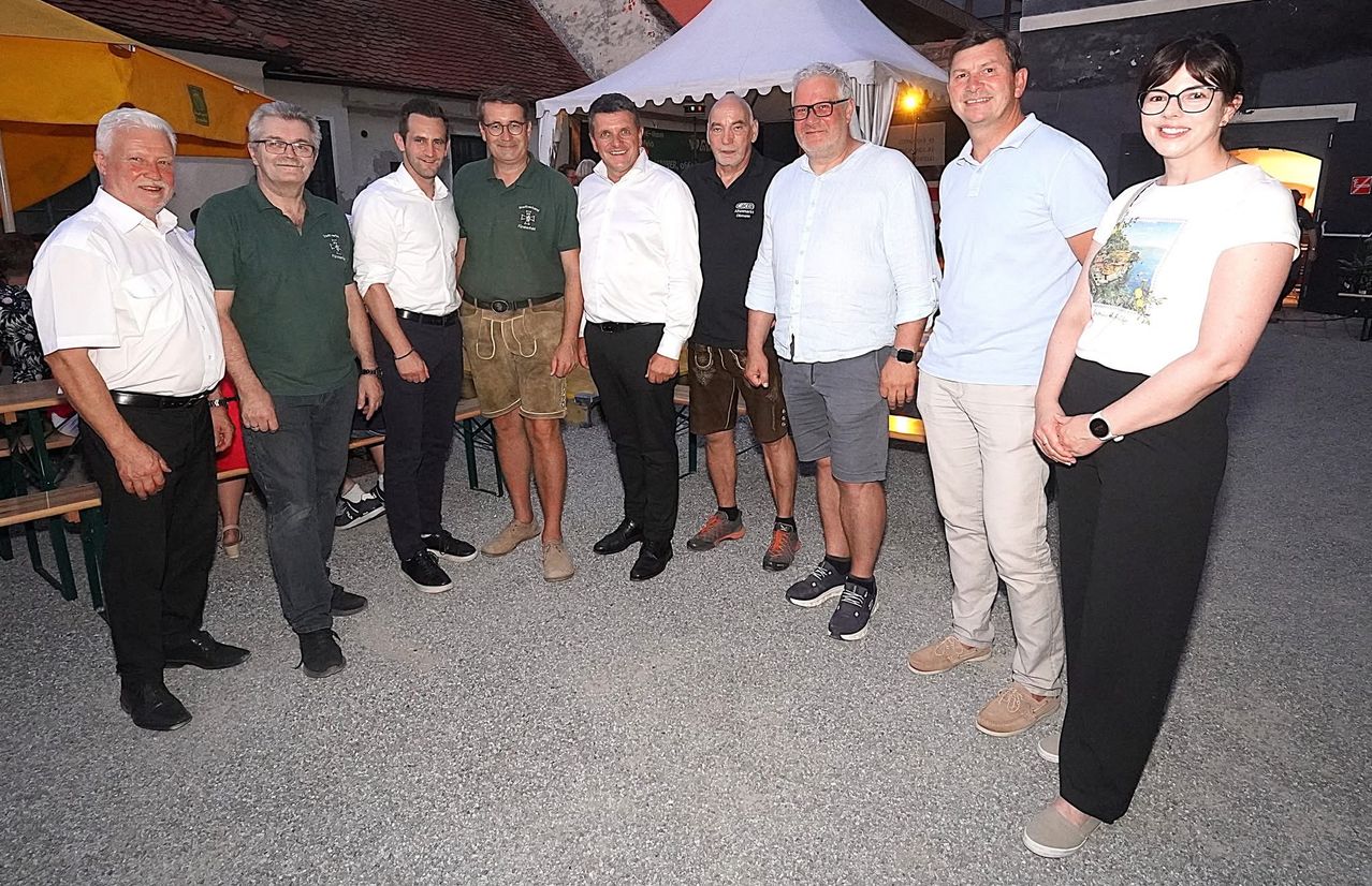 Eine Gruppe von Männern in Freizeitkleidung steht draußen zusammen, möglicherweise bei einer Veranstaltung. Einer trägt ein grünes Shirt, ein anderer ein weißes und andere in Schwarz und Beige.