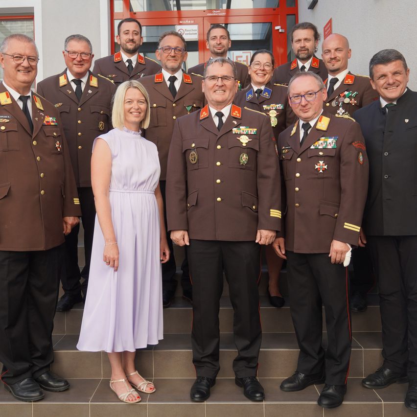 Eine Gruppe uniformierter Männer und eine Frau in einem Kleid posieren für ein Foto auf Stufen. Die Männer tragen Medaillen und Mützen, und die Frau lächelt.