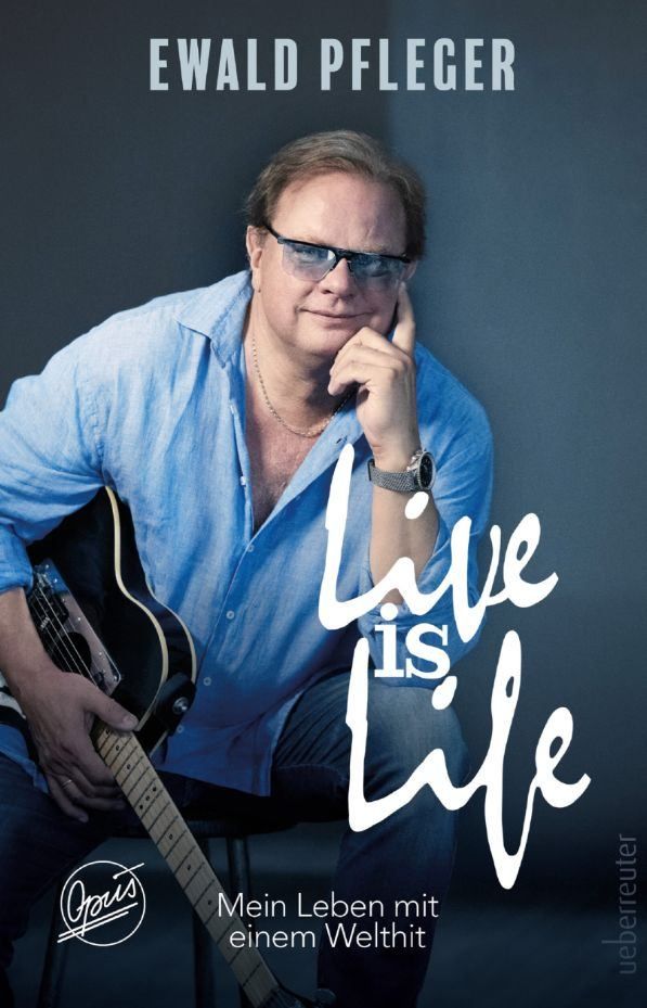 Ein Mann in einem blauen Hemd hält eine Gitarre und sieht nachdenklich aus. Das Bild zeigt den Text 'Live is Life', was auf ein Thema der Lebensfreude hinweist.
