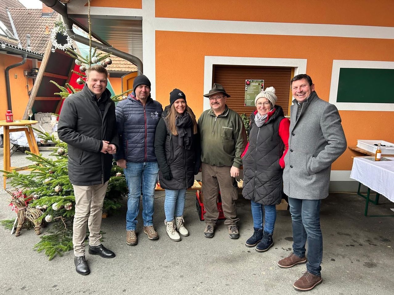 Eine Gruppe von Menschen steht vor einem dekorierten Gebäude und lächelt für ein Foto. Sie tragen alle Winterkleidung.
