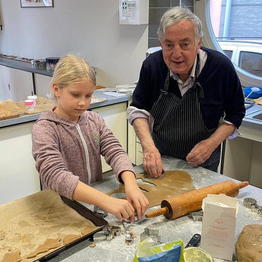 Ein älterer Mann und ein junges Mädchen backen Lebkuchen in der Küche. Sie verwenden einen Nudelholz und Ausstechformen.