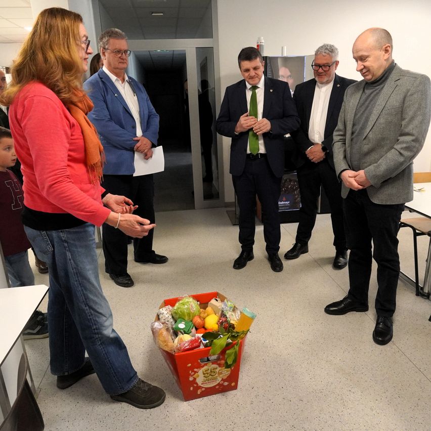 Eine Gruppe von Menschen ist in einem Raum versammelt. Sie scheinen über eine rote Box mit Lebensmitteln zu sprechen.