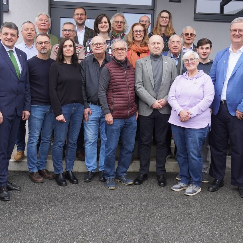 Eine Gruppe von Erwachsenen, einige mit Brille, posiert für ein Foto vor einem Gebäude.