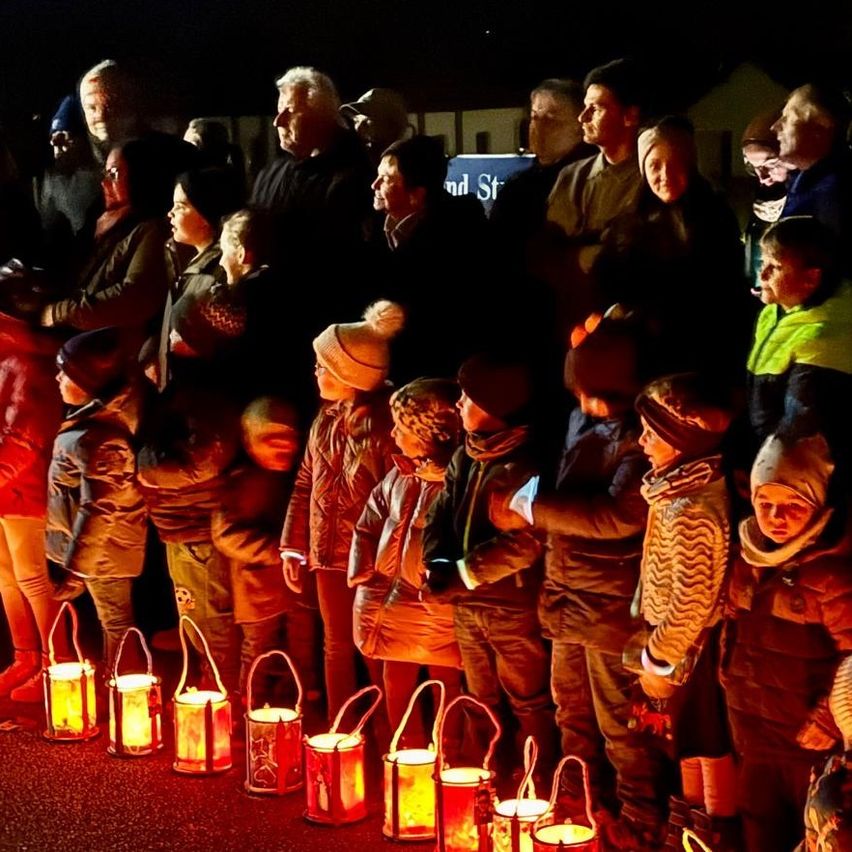 Eine Gruppe von Menschen steht bei Nacht draußen und hält brennende Laternen. Einige Erwachsene sind anwesend und Kinder stehen davor.