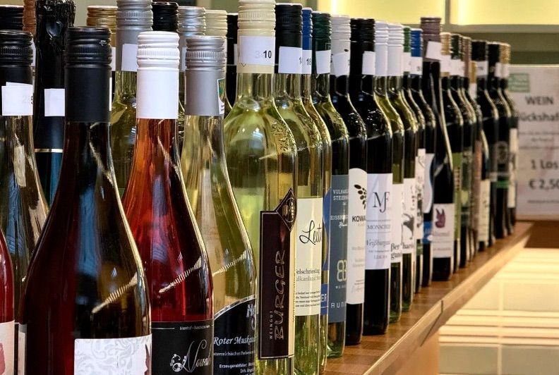 A row of wine bottles on a wooden shelf, some labeled with numbers and letters.