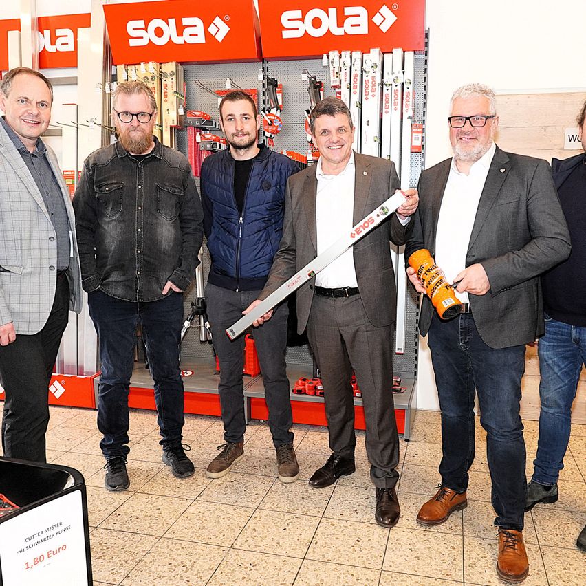 Fünf Männer stehen vor einem Sola-Geschäft, einer hält ein Sola-gebrandetes Werkzeug. Sie alle lächeln und scheinen für ein Foto zu posieren.