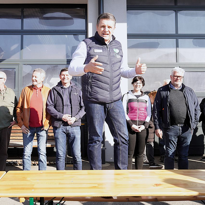 Ein Mann steht auf einem Tisch und hält eine Rede, während andere um ihn herum stehen. Dahinter befindet sich eine Glaswand mit Reflexionen.