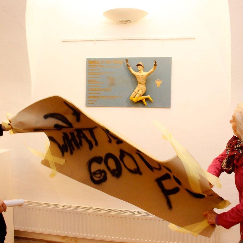 Zwei Personen halten ein großes Stück Papier mit den Worten 'Oh was für ein guter Kampf!' darauf. Daruber ist ein Bild von einem springenden Soldaten.