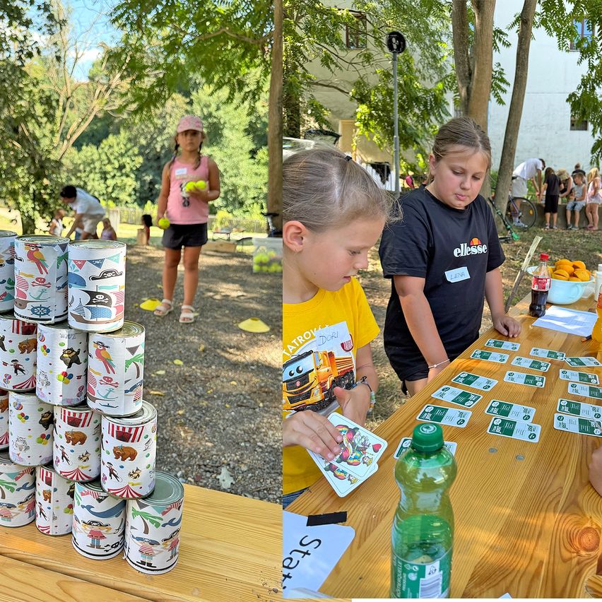 Zwei Kinder spielen ein Spiel mit Karten und Dosen auf einem Tisch im Park. Ein Kind hält eine Karte und schaut sie sich an, während das andere Kind hinter ihr steht.