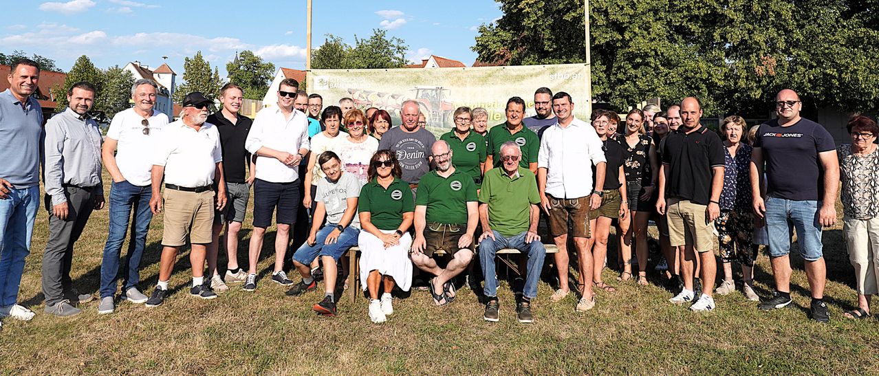 Eine Gruppe von Menschen in grünen Shirts und Shorts posiert für ein Foto vor einem Banner.
