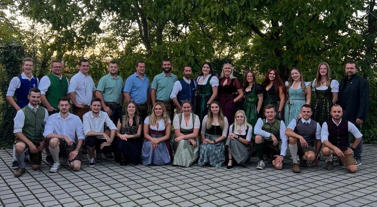 A group of people dressed in traditional German attire are posing for a photo in an outdoor setting.