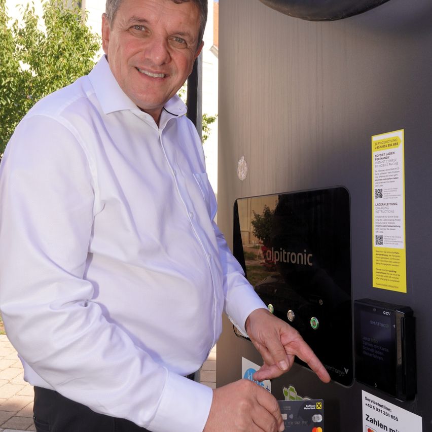 A man in a white shirt is pointing at a charging station with a card in his hand.