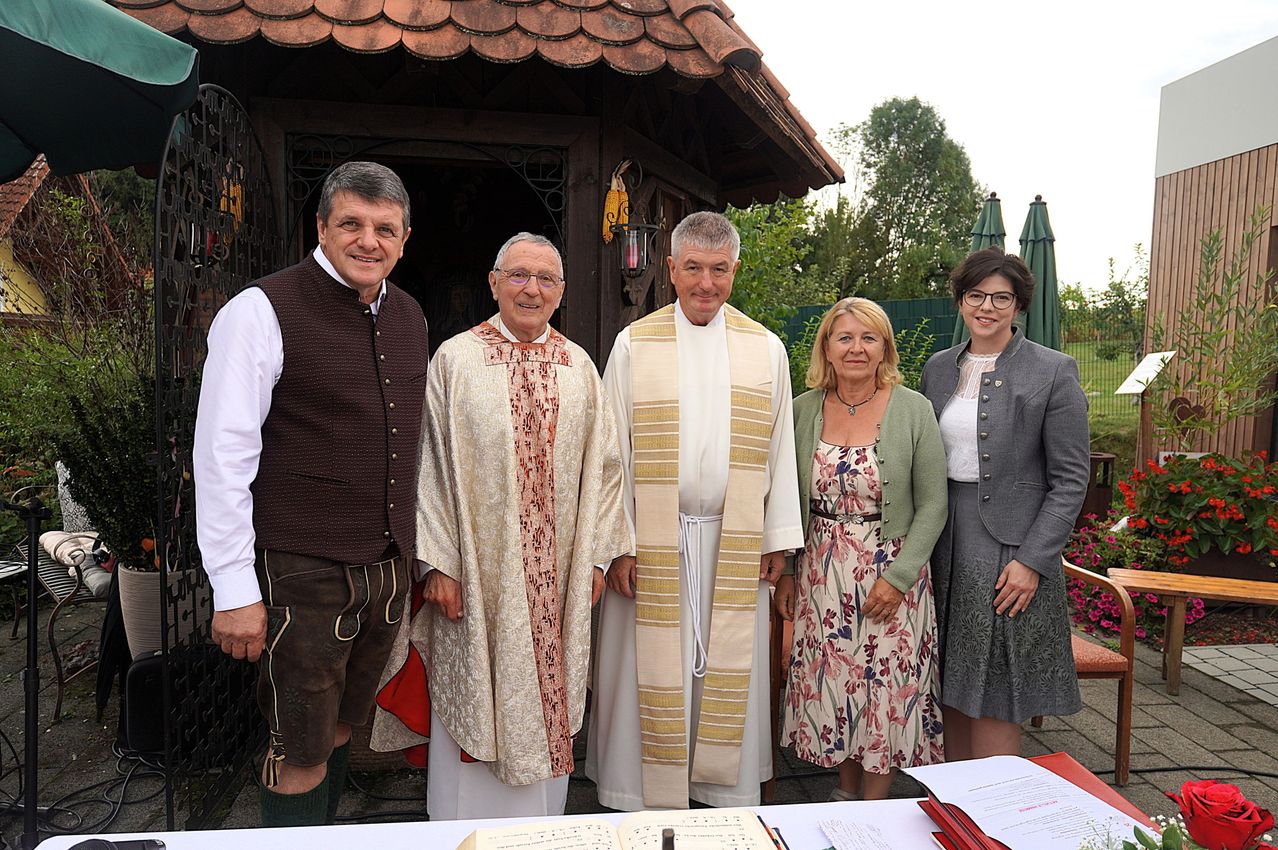 Fünf Personen, darunter zwei Priester, stehen vor einer Kapelle. Sie lächeln und scheinen für ein Foto zu posieren.