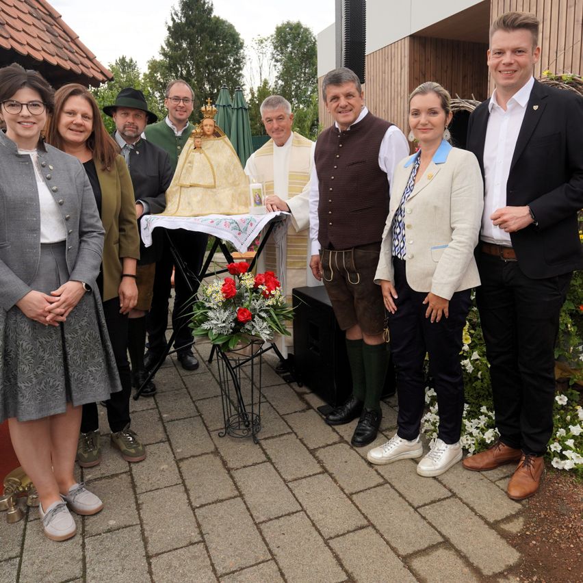 Eine Gruppe von Menschen steht um einen dekorierten Tisch mit einer Statue, möglicherweise bei einer religiösen Veranstaltung.