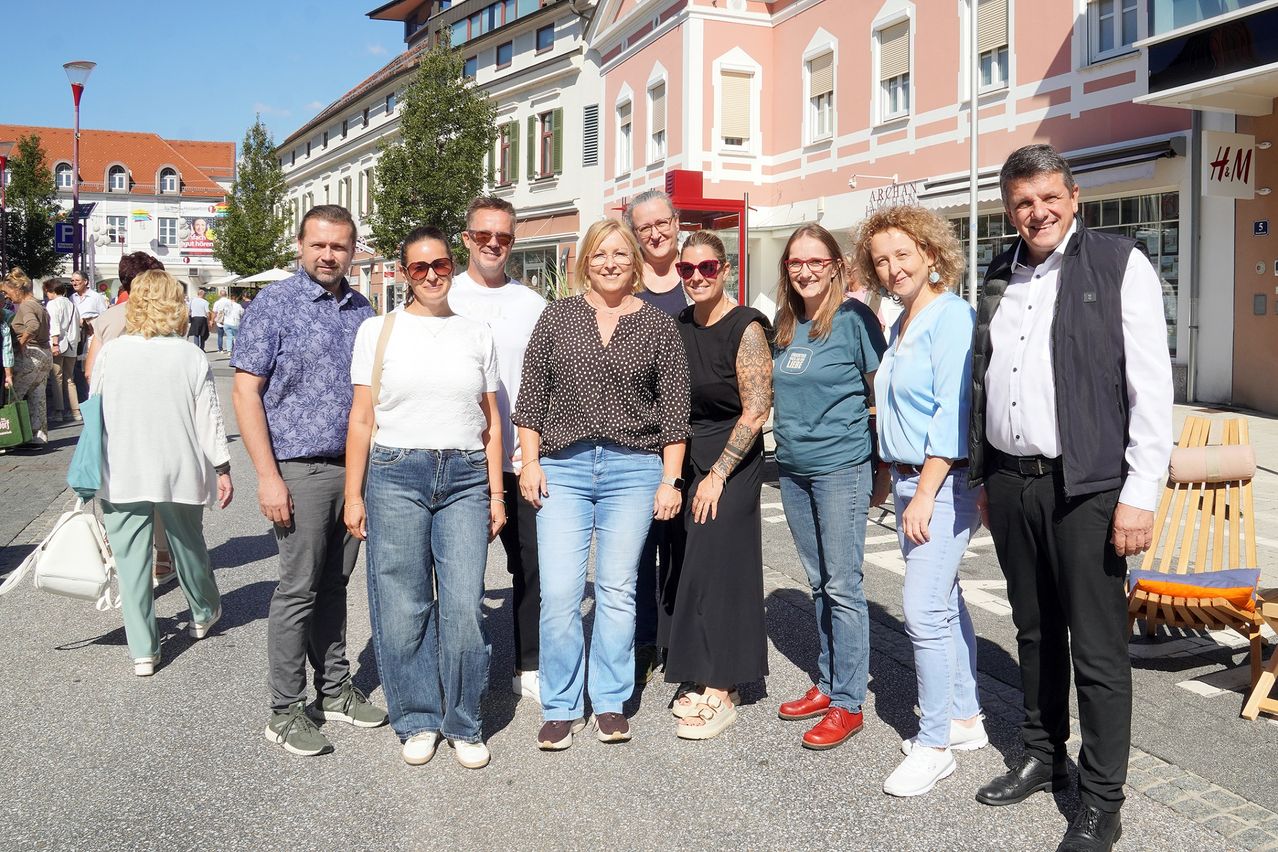Eine Gruppe von Menschen steht vor einem rosa Gebäude und lächelt für ein Foto. Sie tragen Freizeitkleidung und einige von ihnen tragen Brillen.