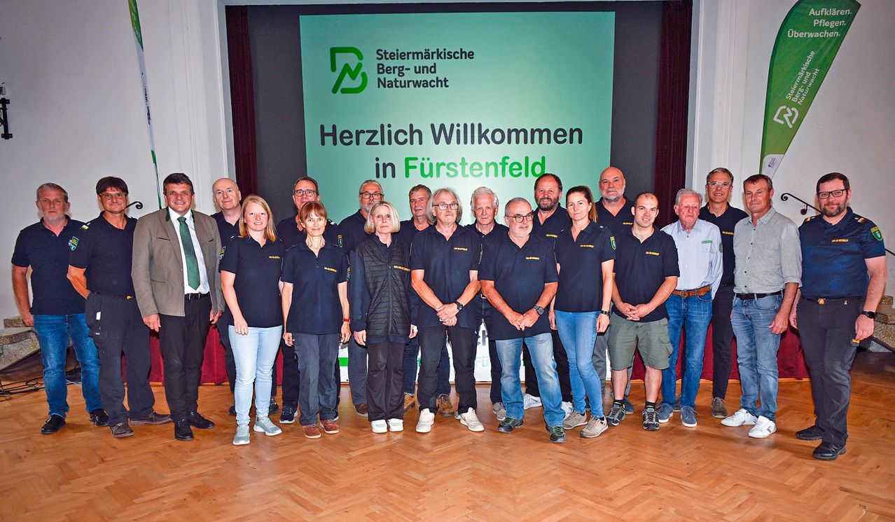 Eine Gruppe von Menschen in Uniform vor einem grünen Banner mit den Worten 'Herzlich Willkommen in Furstenfeld'.