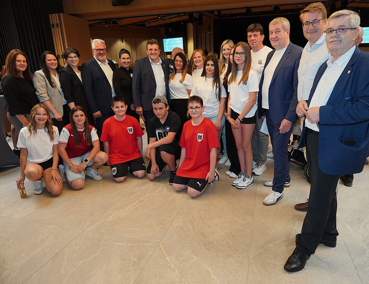 Eine Gruppe von Menschen in formeller Kleidung, darunter ein Junge in Rot, posiert für ein Foto in einem Saal.