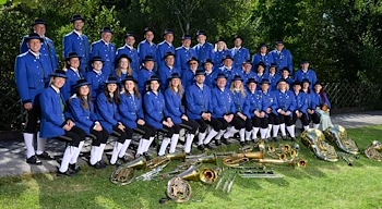 Eine große Gruppe von Musikern in blauen Uniformen und Hüten posiert für ein Foto auf einem Rasenfeld mit verschiedenen Blechblasinstrumenten.
