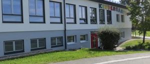 Ein großes weißes Gebäude mit mehreren Fenstern und einer roten Tür. Das Wort 'Kindergarten' ist an der Seite geschrieben.