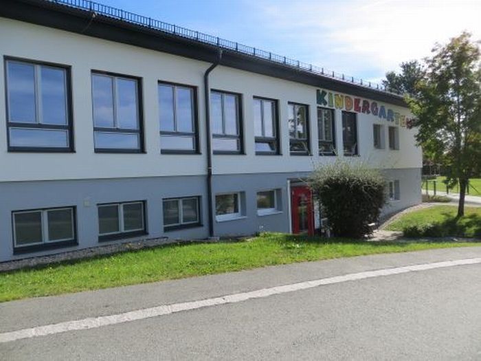Ein großes weißes Gebäude mit mehreren Fenstern und einer roten Tür. Das Wort 'Kindergarten' ist an der Seite geschrieben.