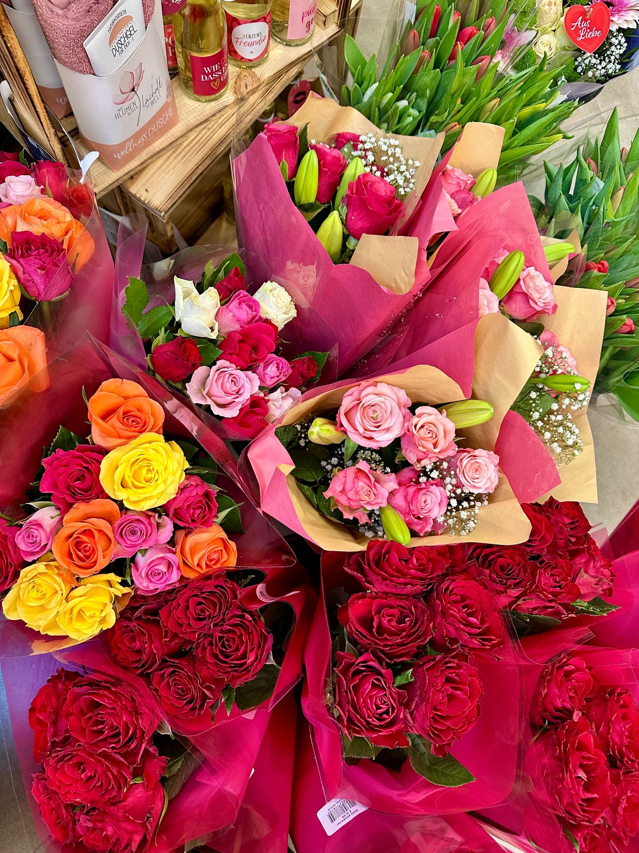 Various bouquets of roses in different colors, such as red, pink, orange, and yellow, are arranged and wrapped in pink and brown paper. They are displayed in a well-organized manner.