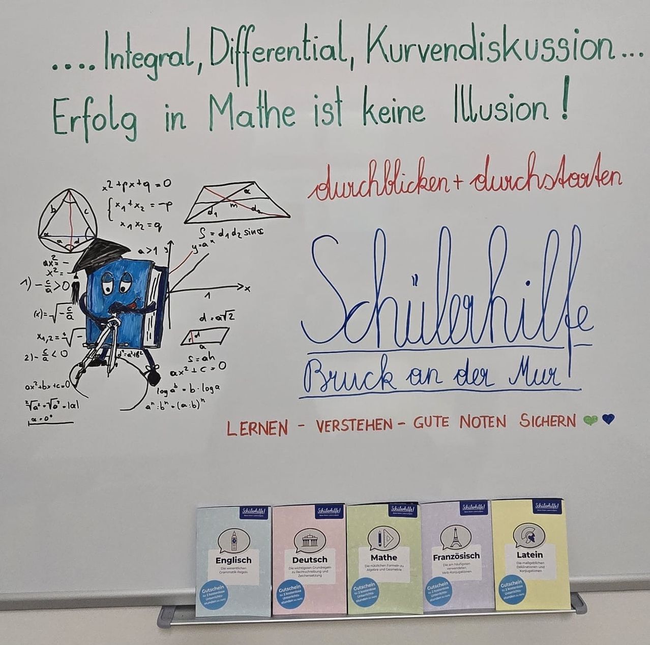 Ein Whiteboard zeigt einen motivierenden Text mit mathematischen Diagrammen und Büchern. Unten sind Broschüren für Englisch, Deutsch, Mathematik, Französisch und Latein.
