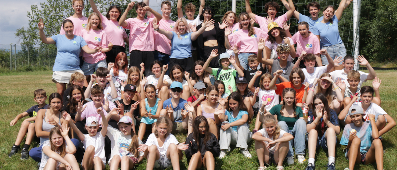 Eine Gruppe junger Menschen in rosa, blauen und weißen T-Shirts, einige mit Mützen, posieren für ein Foto auf einem Rasenfeld mit einem Fußballnetz im Hintergrund.