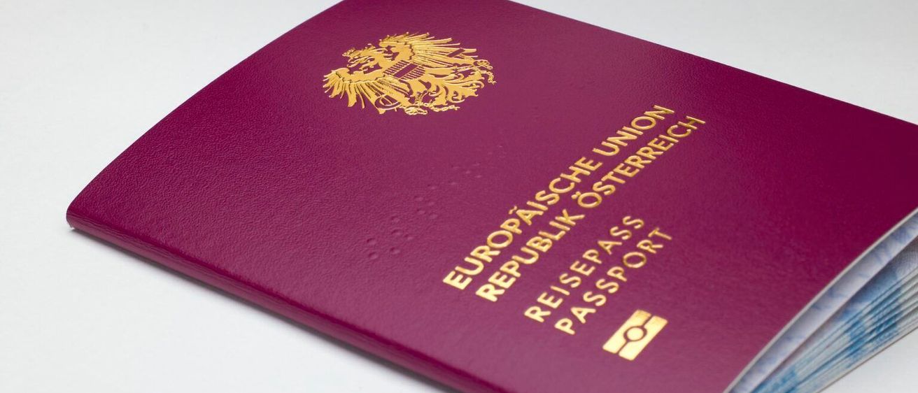 Ein weinroter Reisepass der Republik Österreich mit einem goldenen Emblem und den Worten 'Reisepass' und 'Passport'.