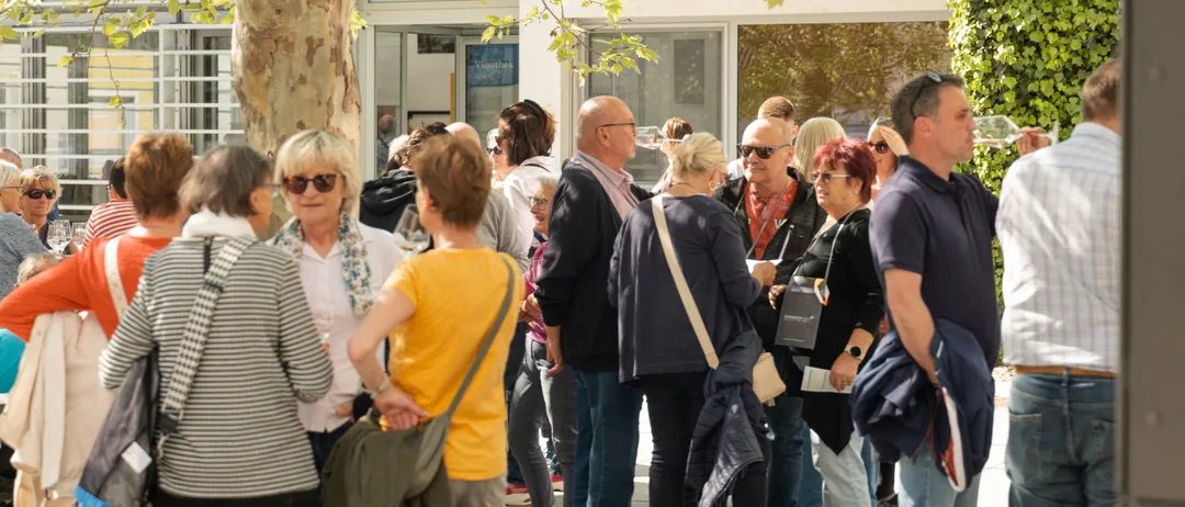 Eine Gruppe von Menschen steht vor einem Gebäude, einige unterhalten sich und andere schauen sich um.