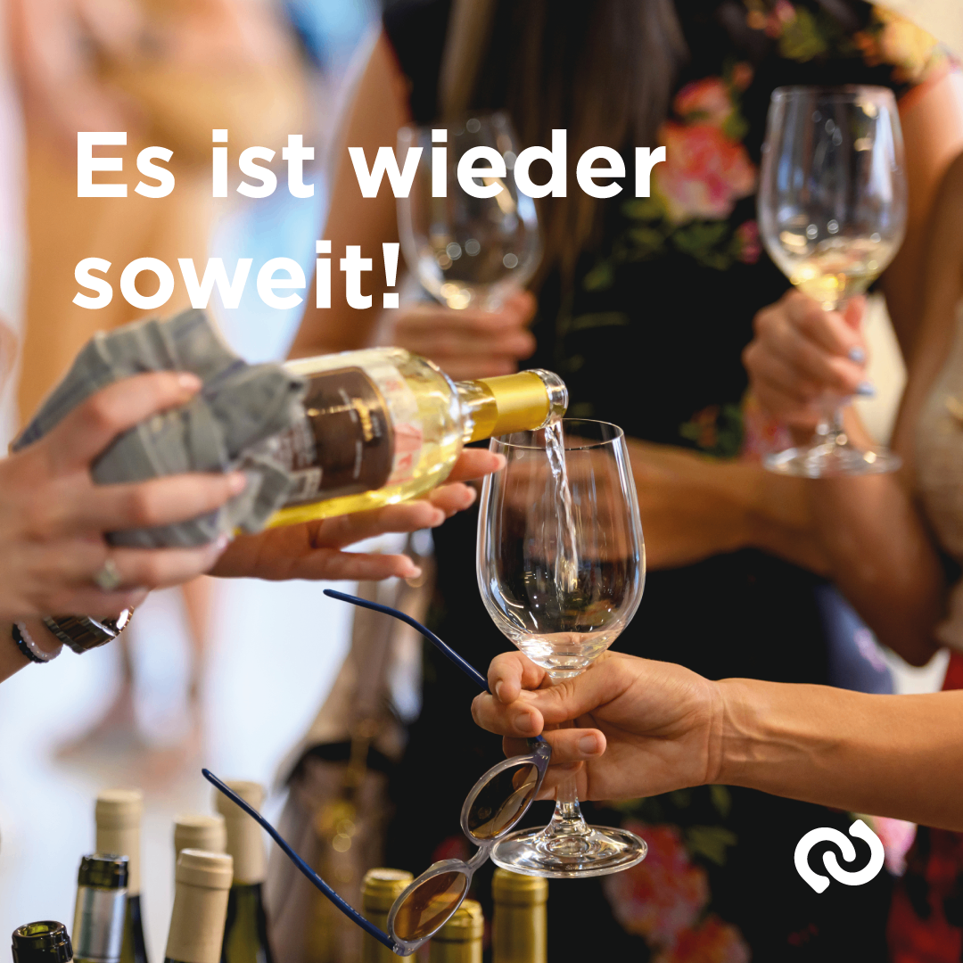 A group of people holding wine glasses are pouring wine into one of the glasses. The text in the image reads, 'Es ist wieder soweit!' in German.