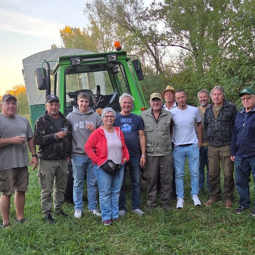 Eine Gruppe von Menschen steht auf einem Feld mit einem Traktor im Hintergrund. Sie sind lässig gekleidet und scheinen für ein Foto zu posieren.